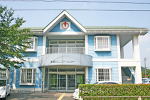 2階建ての白と水色の配色の外壁で玄関入口前に花壇や植樹がされている大塚コミュニティーセンター外観写真