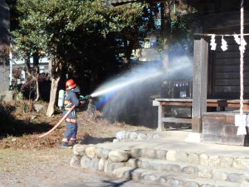 神社内の建物に向かって消防職員が放水をしている様子の写真