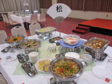 テーブルクロスが敷かれ「松」と書かれた席札テーブルスタンションや料理の品々が並べらている会場の様子の写真