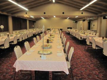 ピンク色のテーブルクロスが敷かれた長テーブルが大勢の人数が収容できるよう縦3列に室内を敷き詰めるように並べられた宴席で利用した会議室の写真