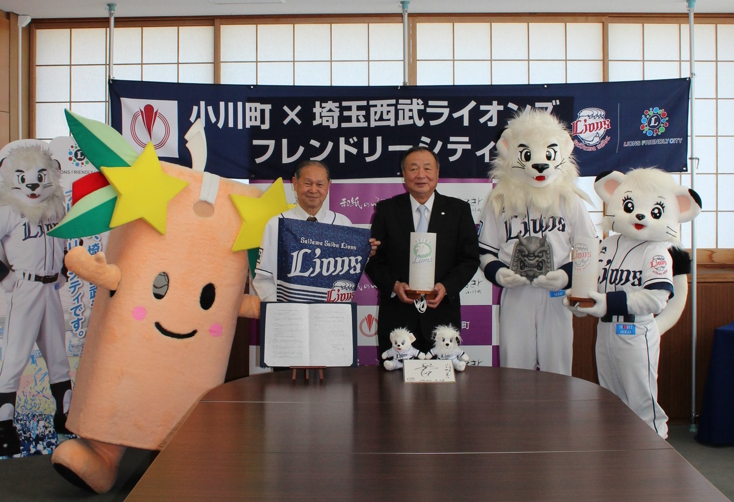 西武ライオンズのユニフォームを着た男性とスーツ姿の男性を中心に星夢ちゃんと球団マスコットのレオとライナが横に並び記念撮影を行っている写真