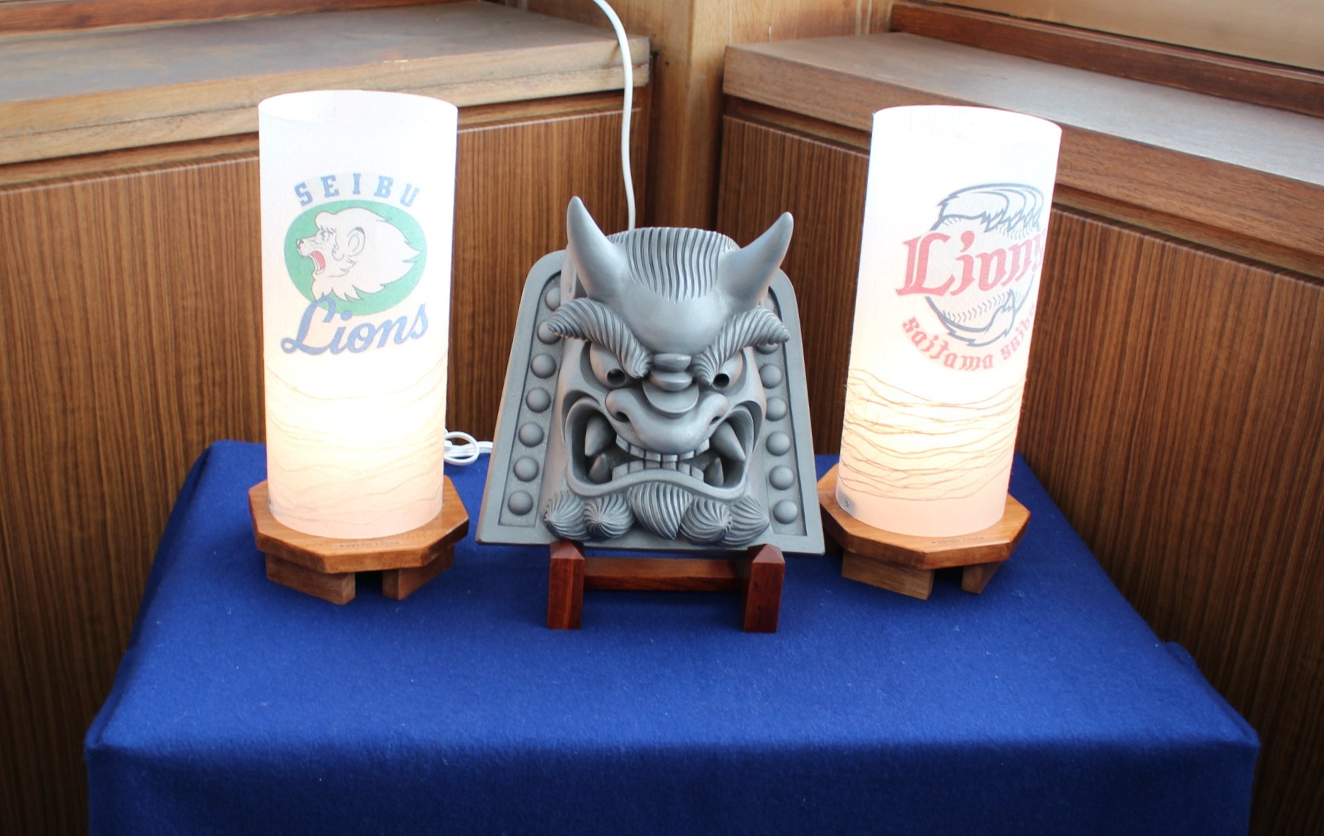 紺色のクロスが敷かれた台に置かれた小川和紙製球団ロゴ入り行灯と富岡鬼瓦の写真