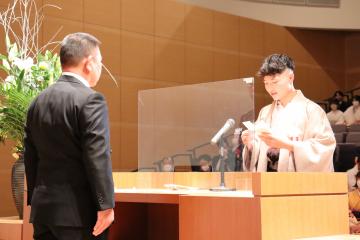 演台をはさみ向かい合わせ立っている町長と式辞表を持ち誓いのことばを述べている羽織袴姿の男性の写真