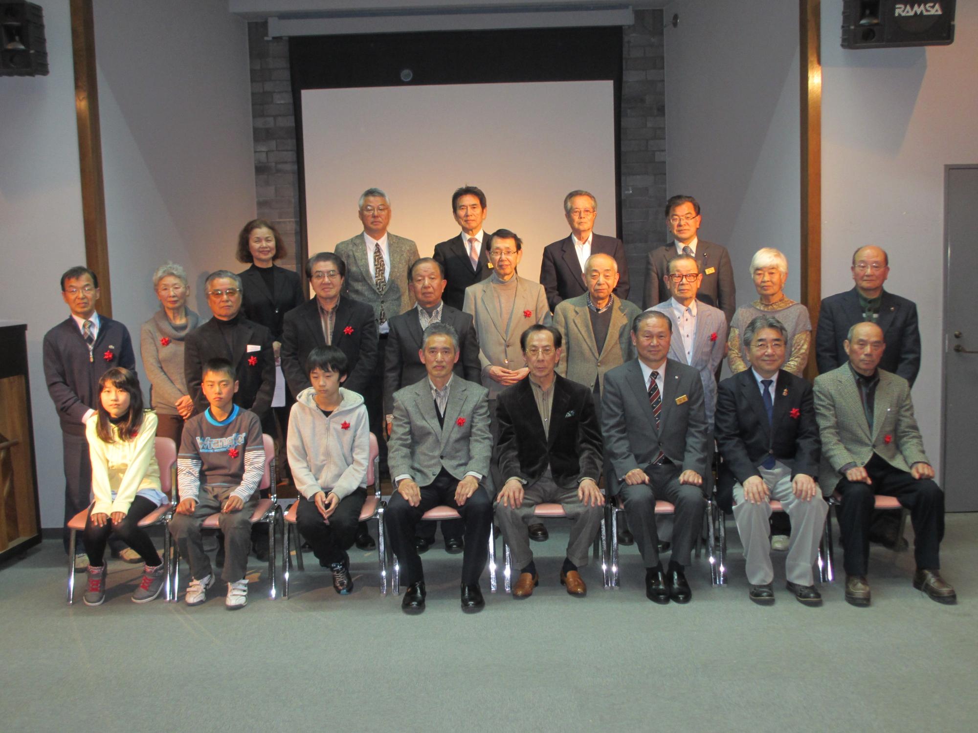 三列に並んだ受賞者の方々と一緒に一列目に座る松本町長との記念撮影の写真