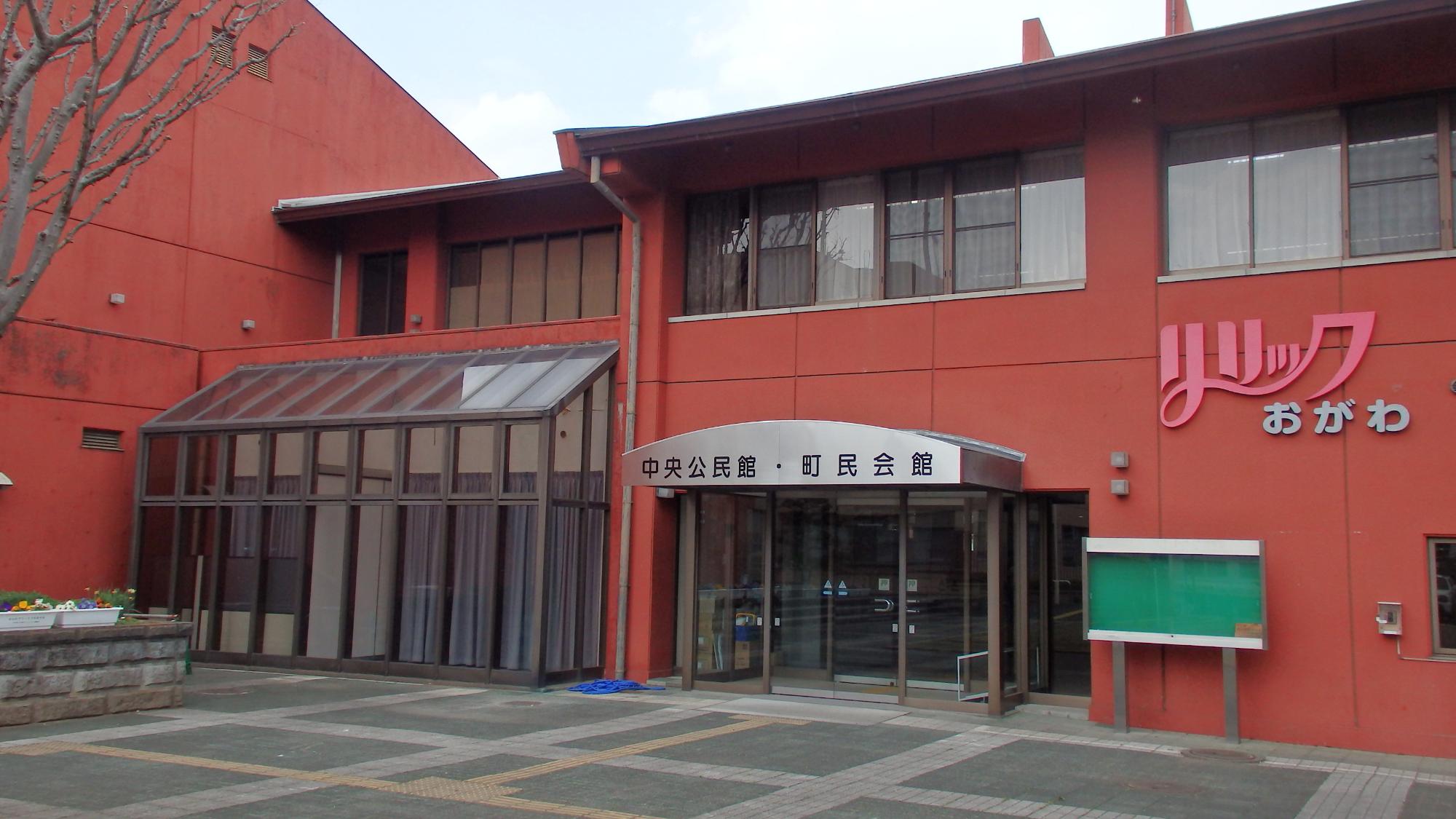 赤茶色の外壁で壁に「リリックおがわ」の壁面看板があり玄関入口には「中央公民館・町民会館」と書かれている中央公民館の写真