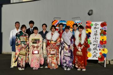 「令和4年小川町成人式」と書かれた立て看板の前で前列に振袖姿の女性5名と羽織袴やスーツ姿の男性5名が記念撮影をしている写真
