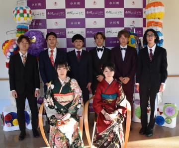 小川市のバックボードを背景に前列に椅子に腰かけた振り袖姿の女性2名と後列にスーツ姿の6名の男性が並んだ記念撮影の写真