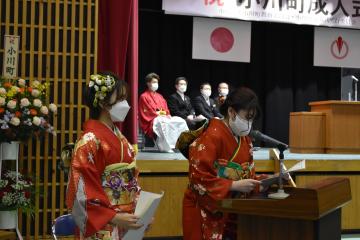 ステージ下に置かれた演台の前でマイクに向かって話をしている様子の振袖姿の女性2名の写真