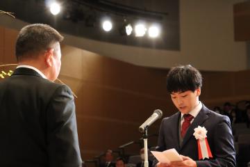 スタンドマイクの前で町長と向かい合わせになり誓いのことばを述べているスーツ姿の男性の写真