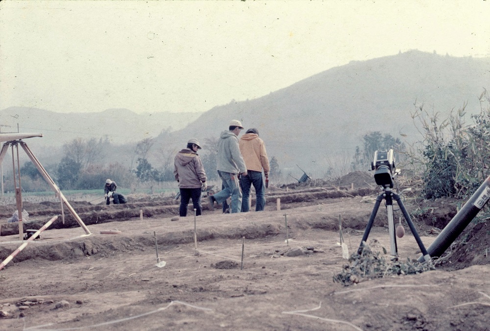 調査用の機材が置かれた土地の一角に作業員数名が立っている写真