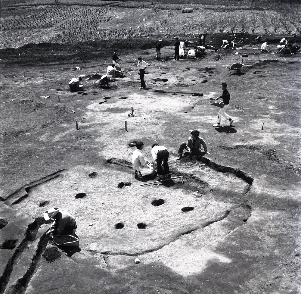 土が掘り起こされ、所々に大小の穴や溝がありその調査を行っている作業員の調査風景の白黒写真