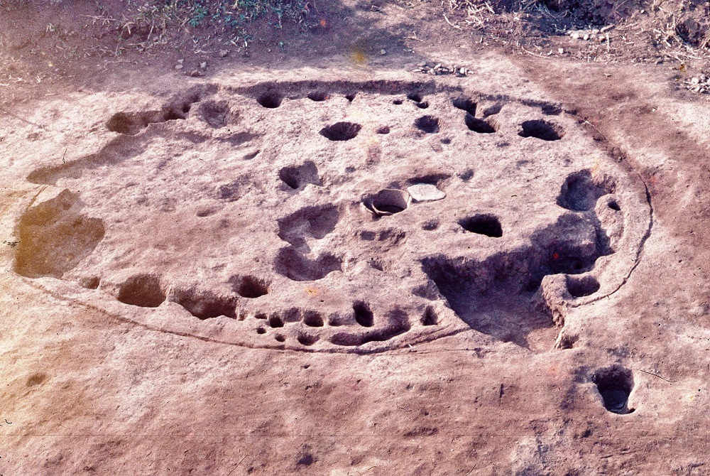 円で囲まれた溝の内側に複数の穴が掘られている住居跡の写真