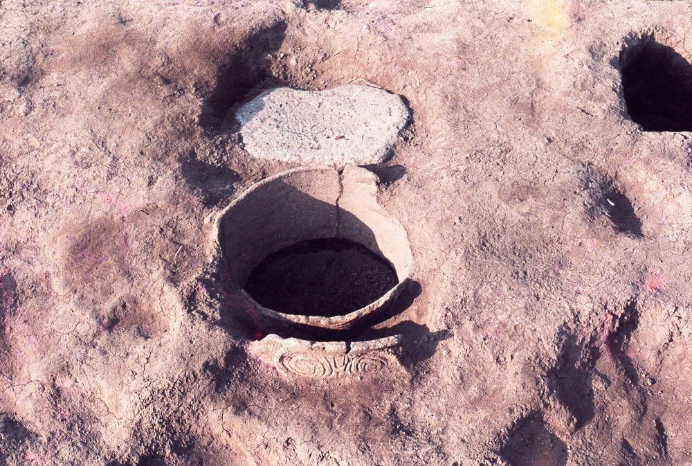 出土された石と穴があいており模様が少し見えている深鉢の写真