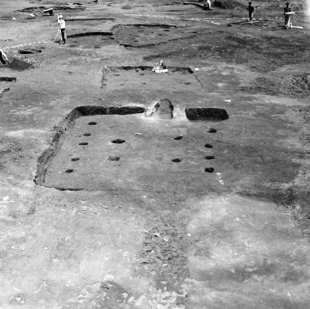 地表面に複数個所のくぼみや穴が開いていたり四角で囲った跡がある箇所で数名の作業員が道具を用いて調査行っている写真