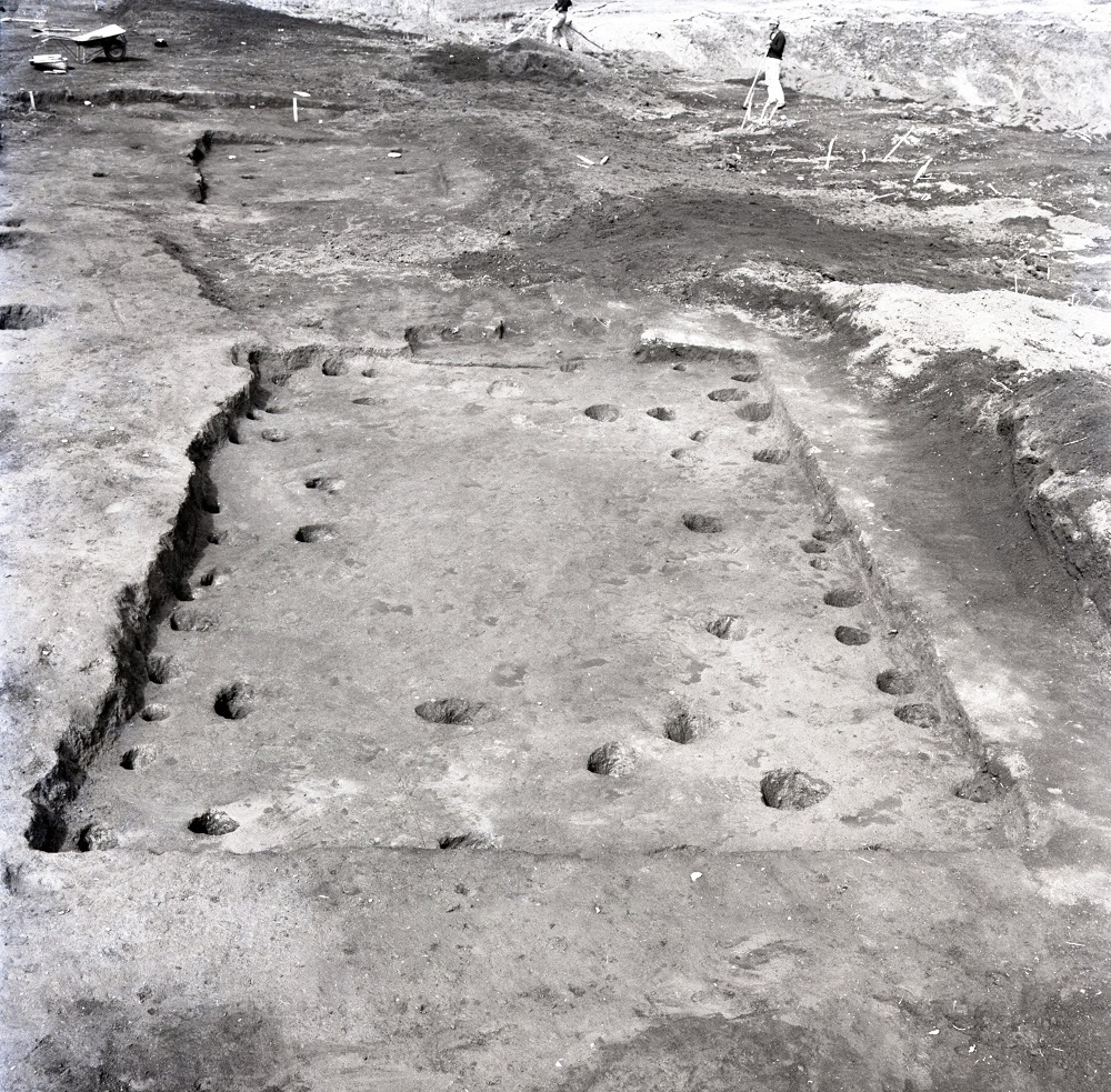 地表面に複数個所のくぼみや穴が開いておりその箇所を四角で囲った跡がある18号住居跡周辺で作業員が調査を行っている写真