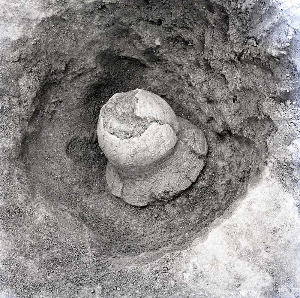 大きな穴の中から出土されたひび割れているが形をのこしている土器の写真