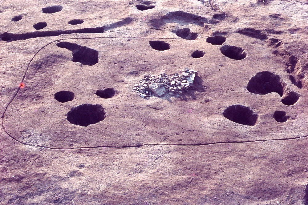 細かな石が密集して置かれておりそのまわりを囲むように穴が点在している土壙の写真