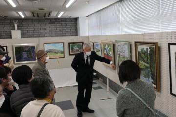壁に展示された作品を新井政明先生が参加者に作品講評をしている様子を写した写真