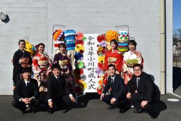 「令和4年小川町成人式」と書かれた立て看板を中心に前列にスーツ姿の男性4名が座り後列に振袖姿の女性5名が立っている記念撮影の写真