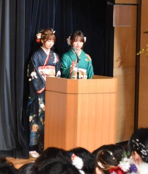 演台に置かれたスタンドマイクの前で振り袖姿の女性2名が立っている写真