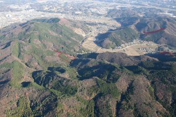 住宅や田畑が後方に見え、連なった山々が前方にみえている遺跡周辺を上空から撮影した写真
