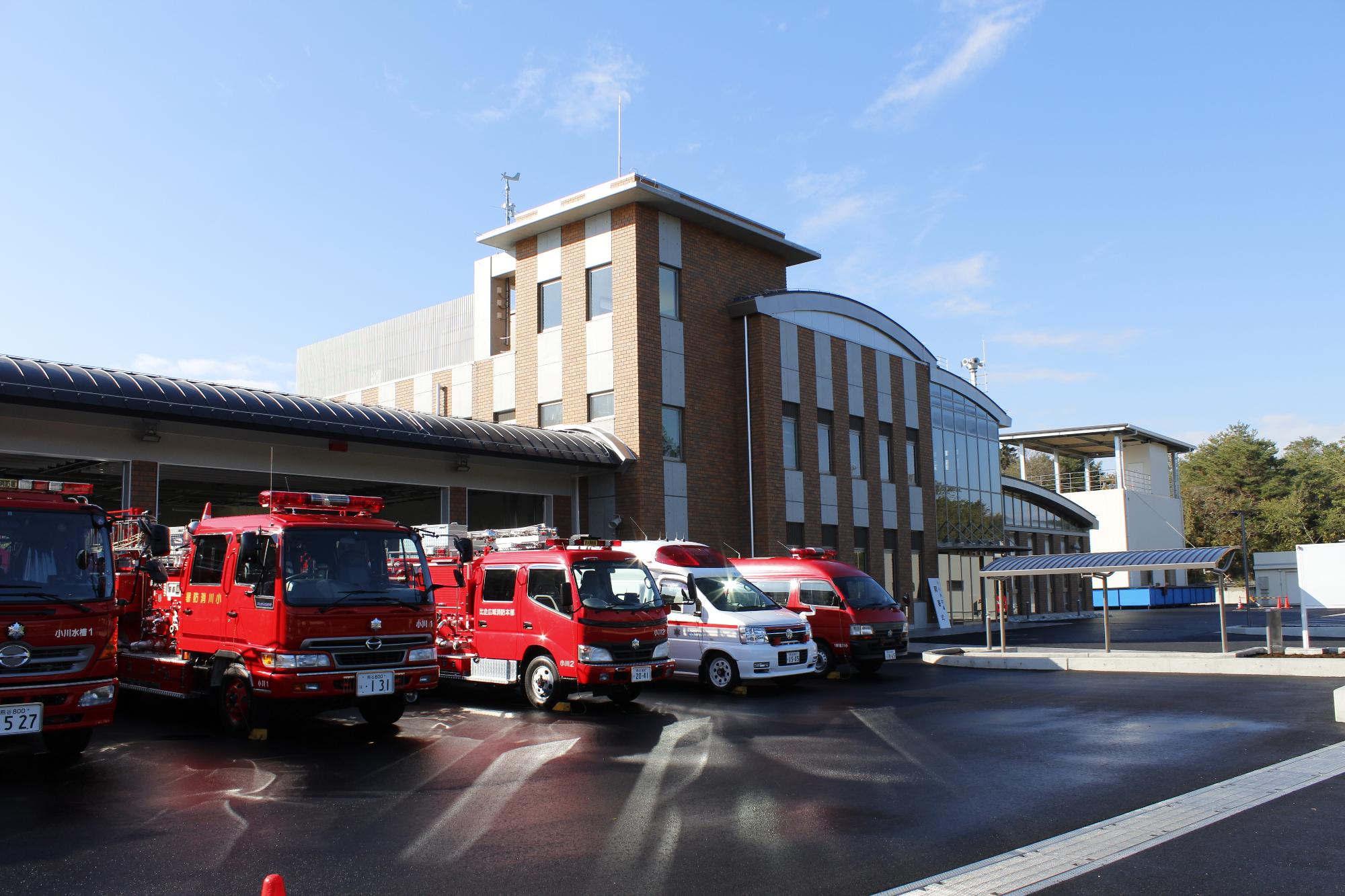 レンガ調と白色の壁で3階建ての建物の前に4台の消防車と1台の救急車が駐車している比企広域消防本部小川消防署の写真