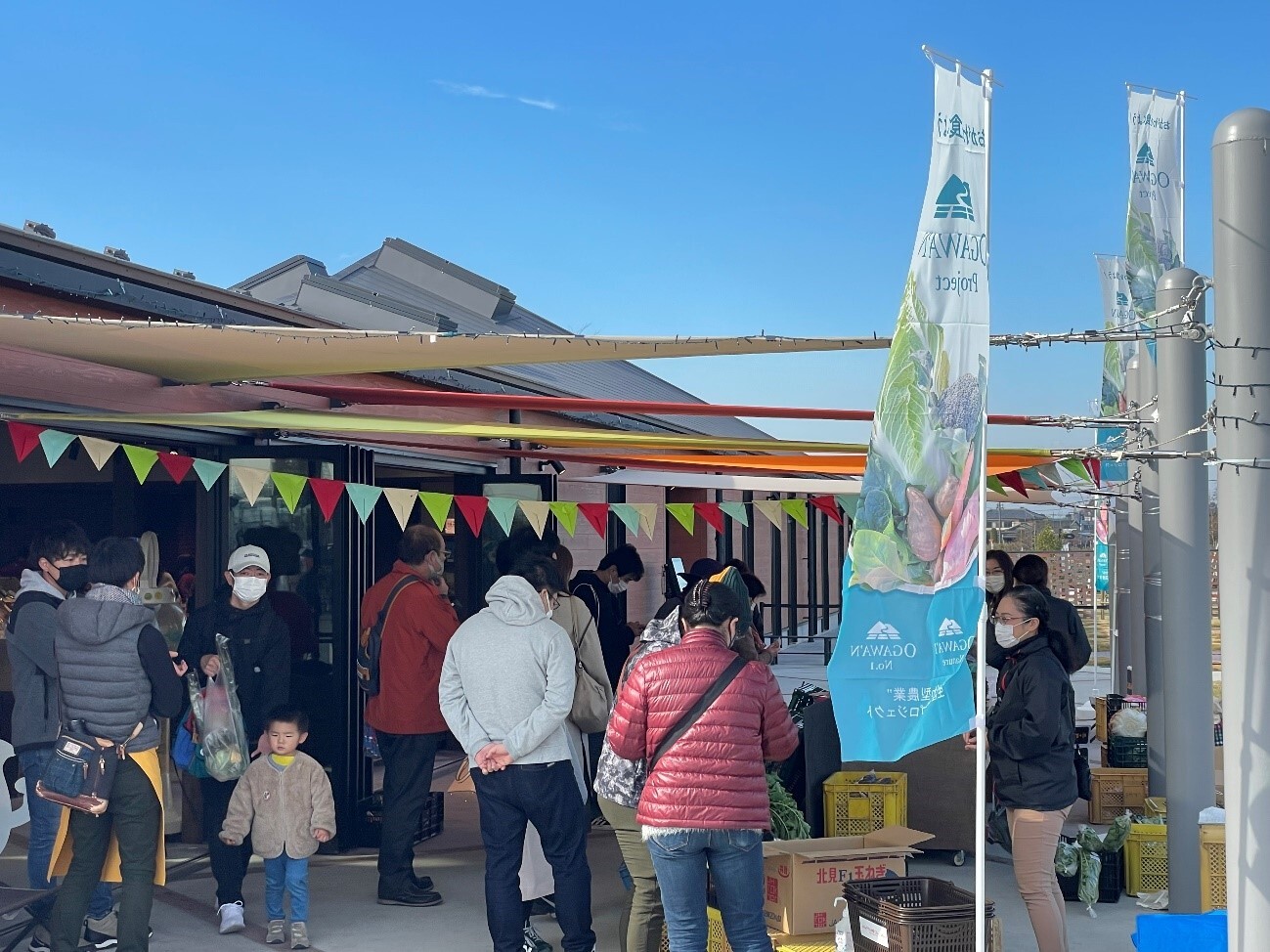 のぼり旗が立っている会場に沢山のお客さんが集まっているマルシェの様子の写真
