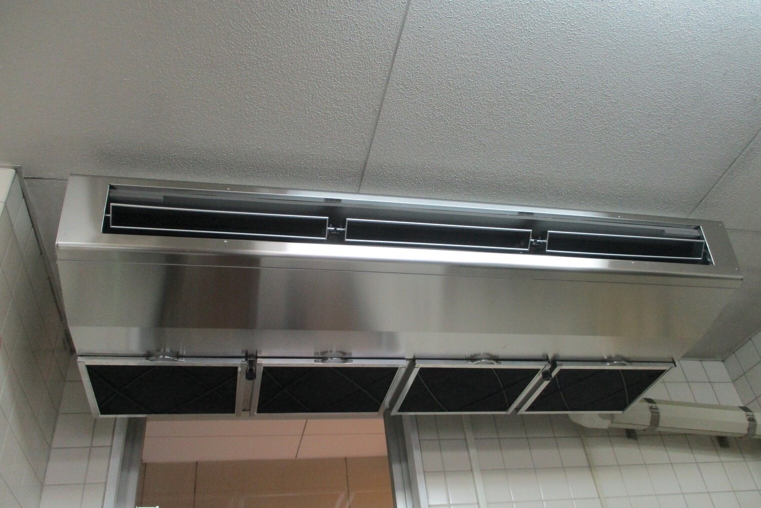 タイル張りの壁の室内の天井に設置された大きな空調機器の写真