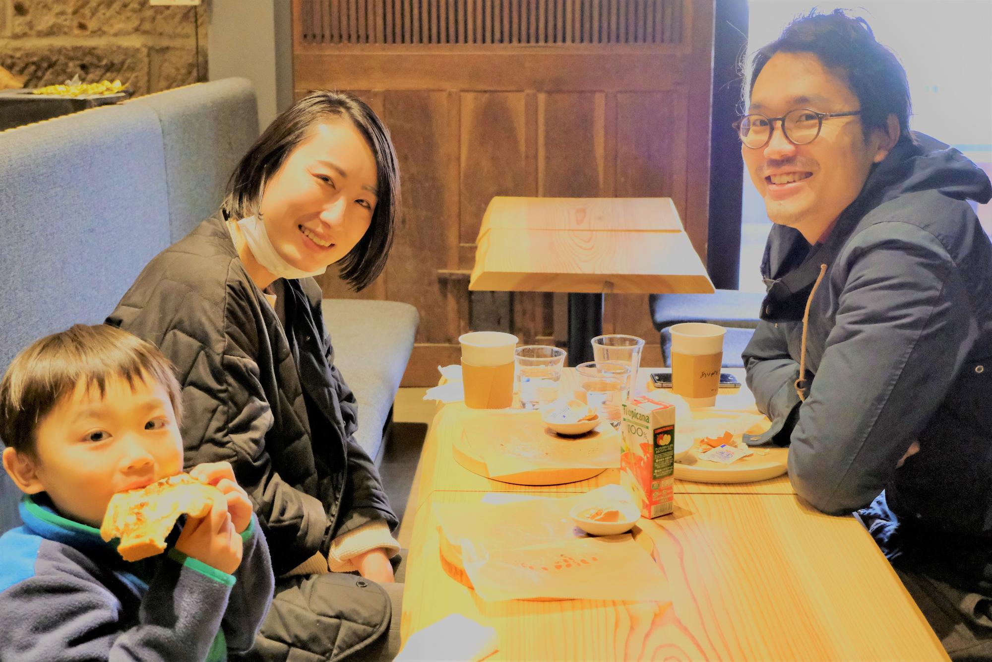 テーブルの席に座った食事を楽しんでいた両親と男の子の家族がカメラに向かって笑顔を向けている写真