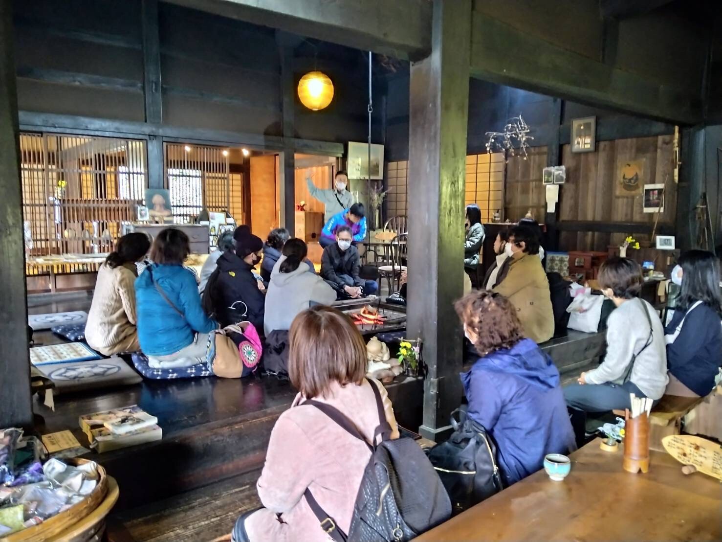 古民家内で前方に立つ男性の話を床に座った参加者が聞いている後ろ姿の写真