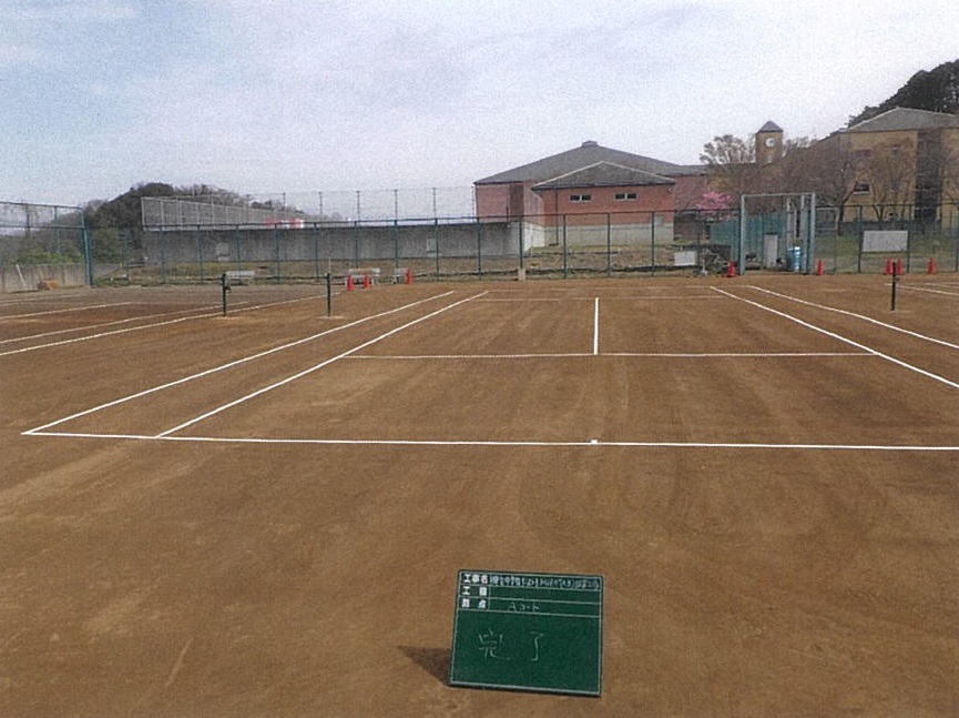 完了と書かれた工事用黒板が、整備されたテニスコート上に置かれている写真