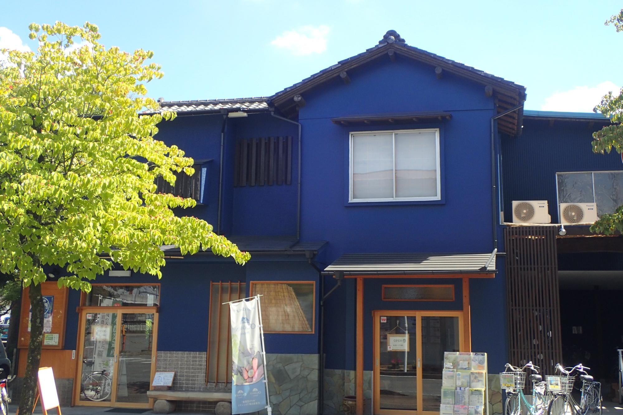 入り口前に2台のレンタサイクルやパンフレットスタンドが設置された、青色の壁の2階建ての建物外観の写真