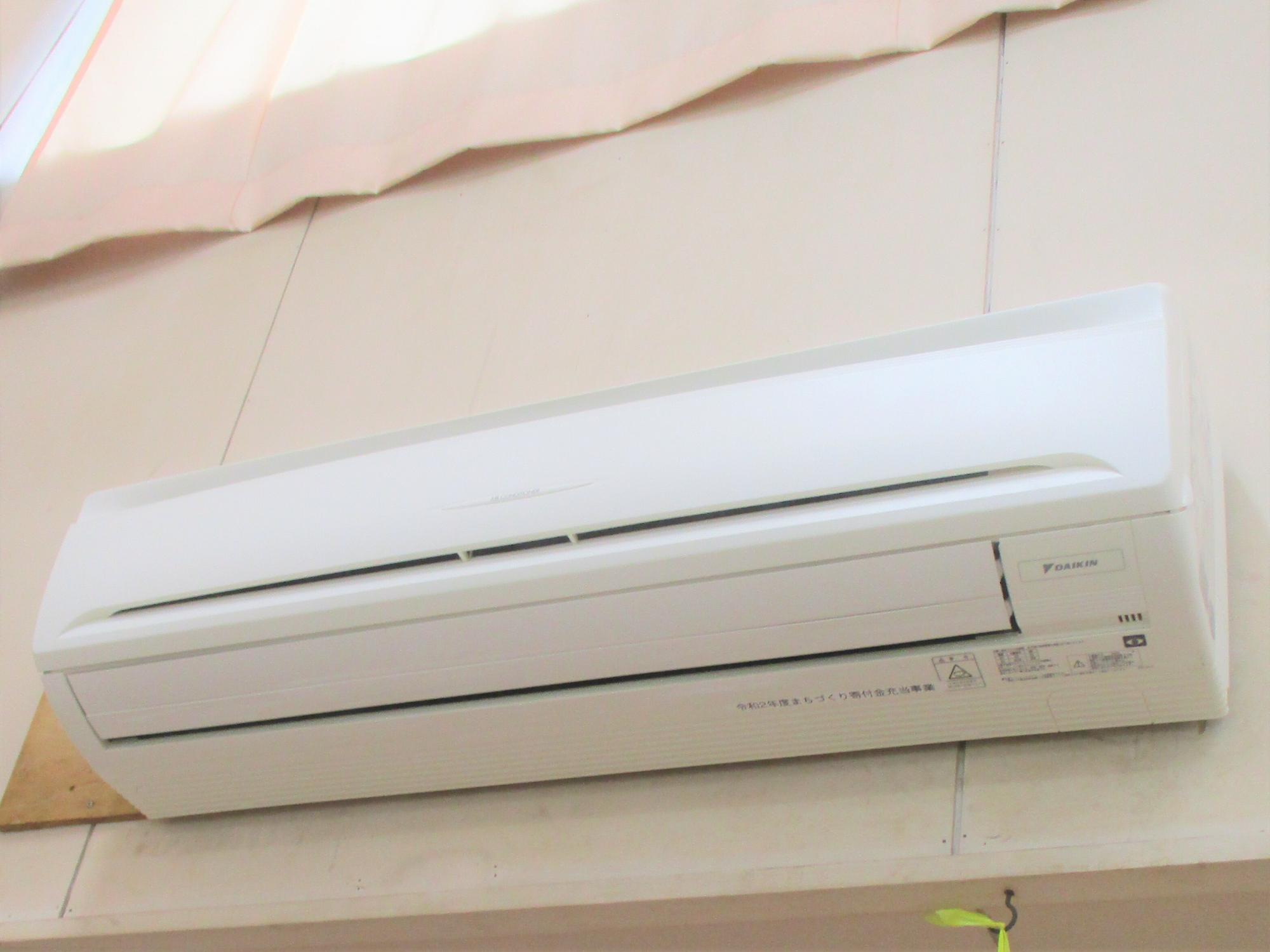 薄いピンク色のカーテンがかかっている下の壁に設置されたエアコンの写真