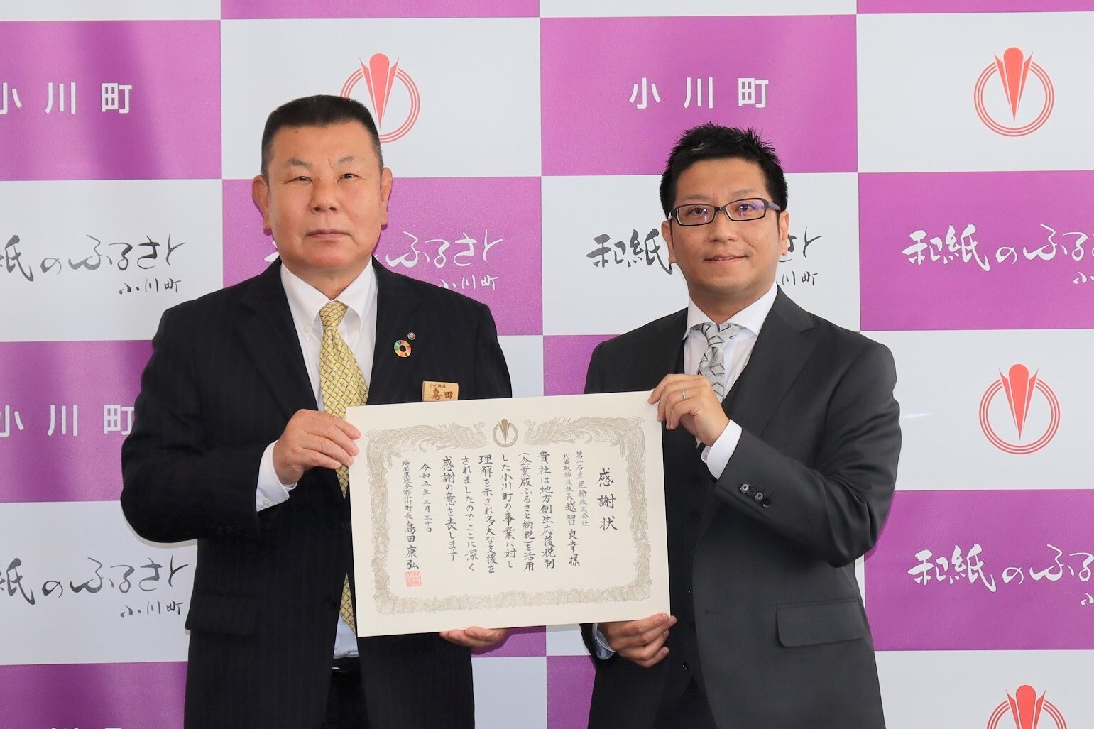 小川町のバックパネルの前で、第一石産運輸の越智副社長と島田町長が一緒に感謝状を持っている贈呈式の様子の写真
