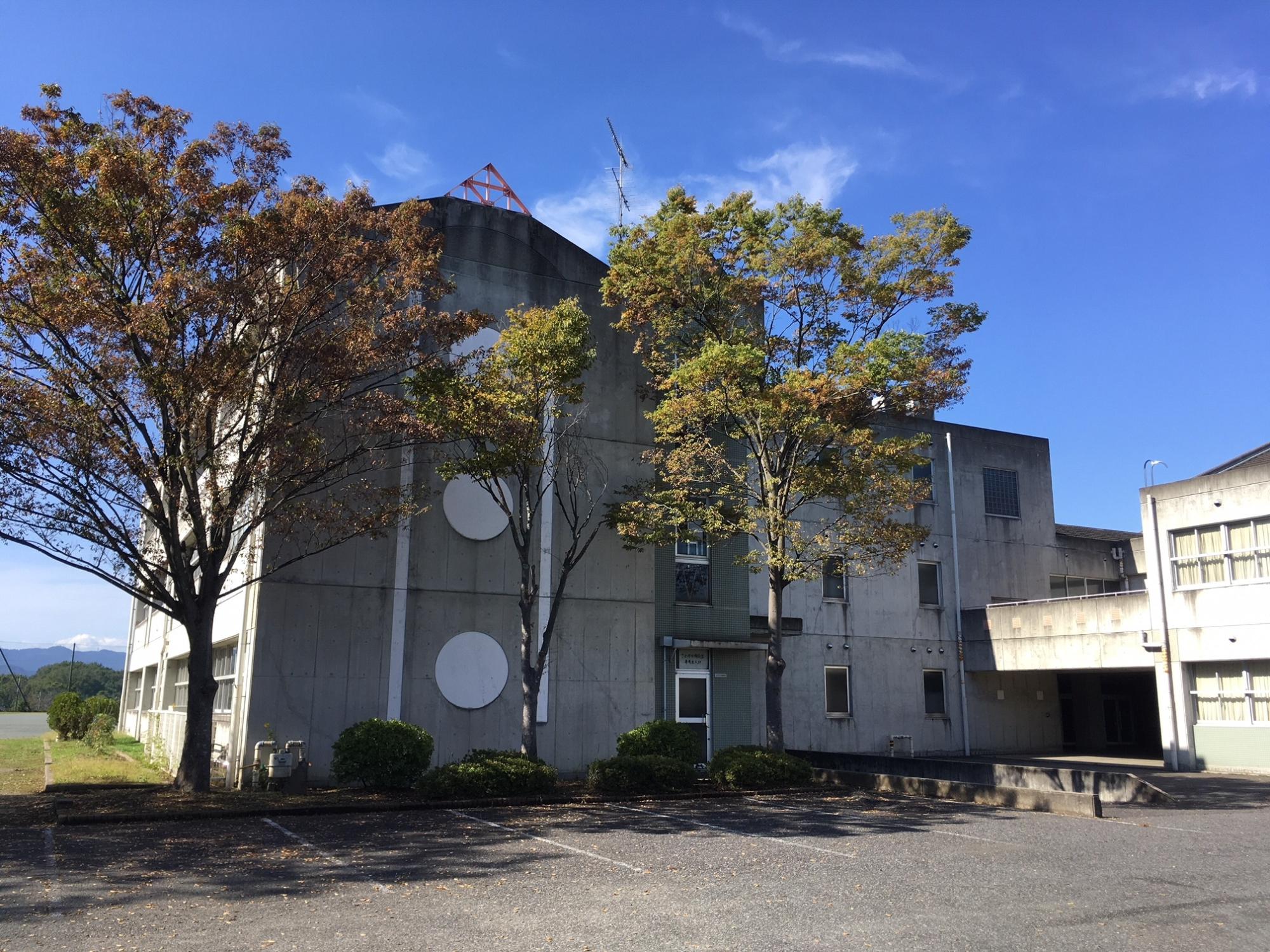 コンクリート造りの壁側面中央に大きな白色の円形のデザインが施された3階建ての校舎棟の外観の写真