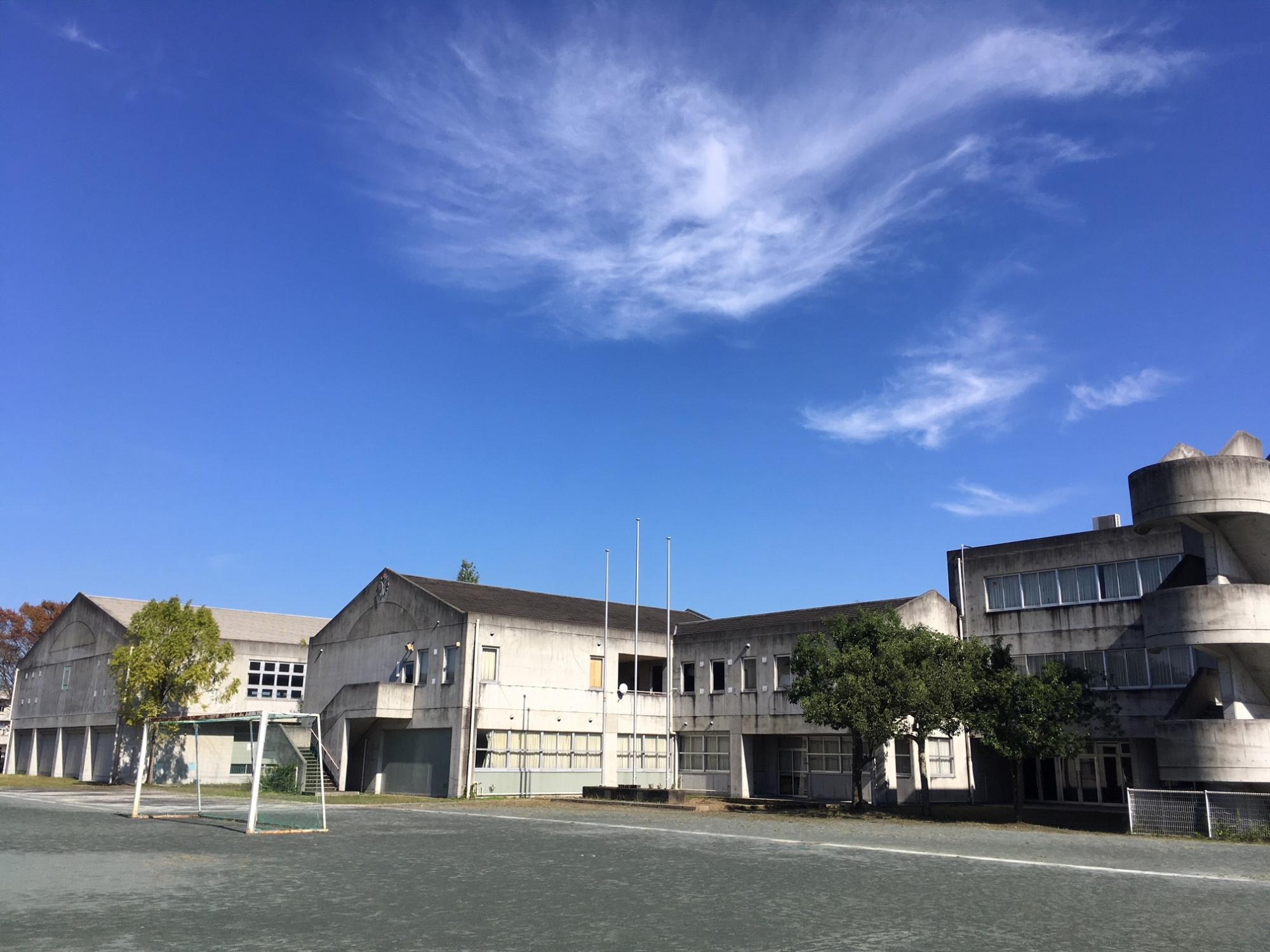 校庭にサッカーのゴールポストが設置され、奥に体育館や3階建ての校舎が建っている旧上野台中学校の敷地内の写真