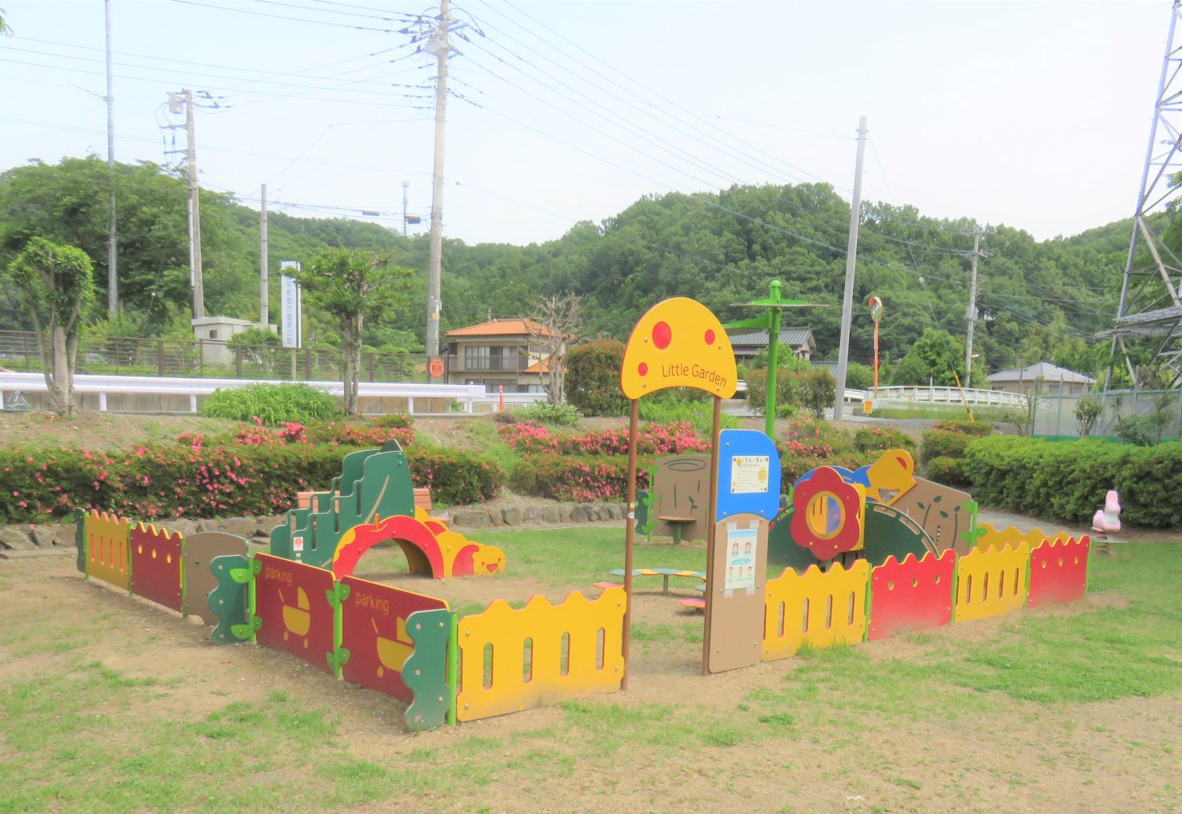 芝生広場に角が丸く作られ黄色や赤色で塗られた木製の柵の中に設置された幼児向け遊具の写真