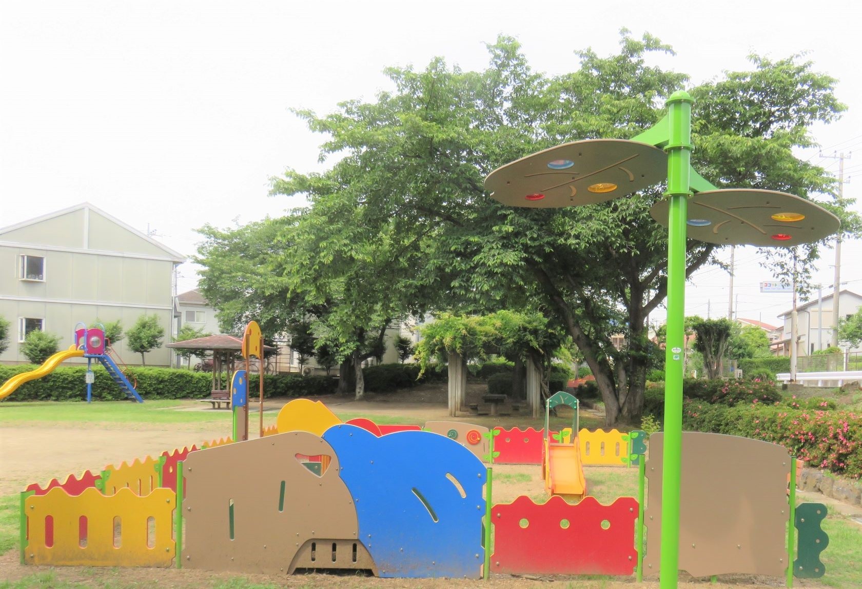 公園内に設置された、角が丸く作られ黄色や青色で塗られた木製の柵の幼児向け遊具の写真