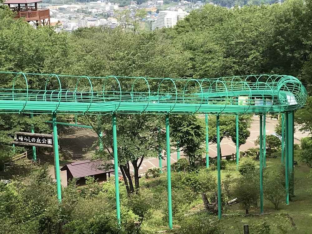 見晴らしの良い公園内に設置された緑色のローラーすべり台を高台から撮影した写真