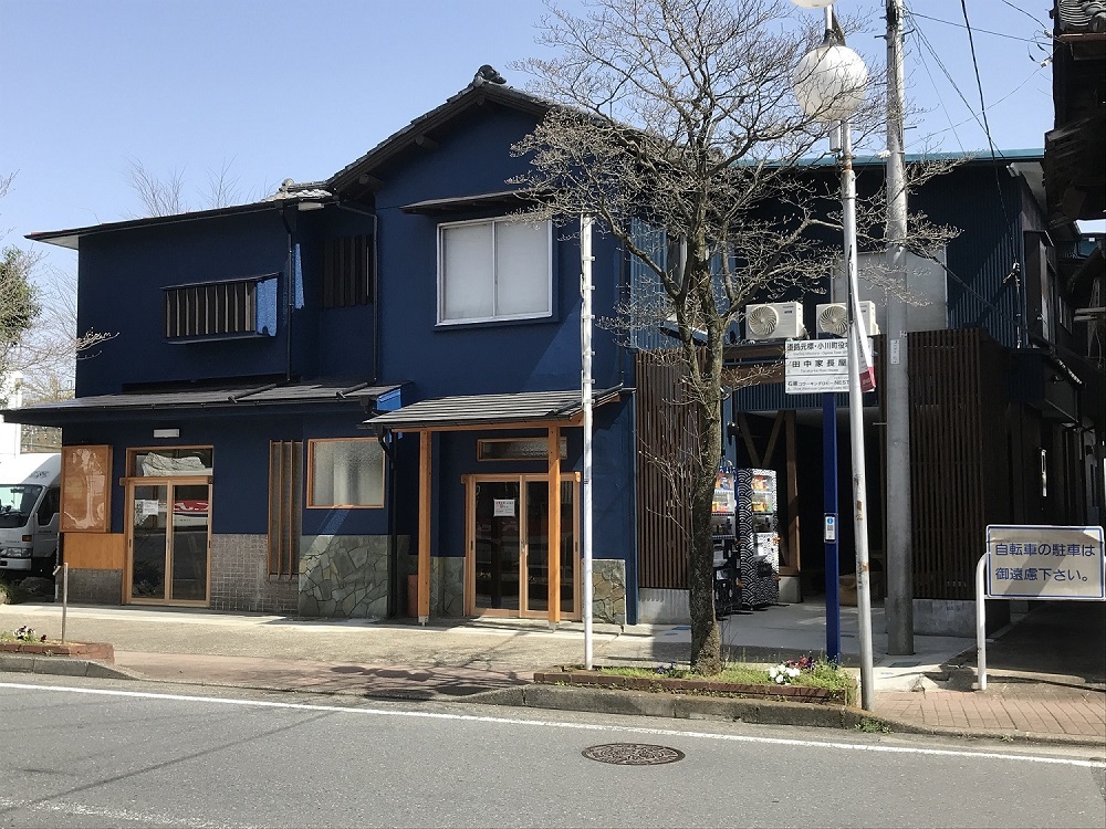 青色の壁で2階建てのむすびめの建物外観を道路の反対側から撮影した写真