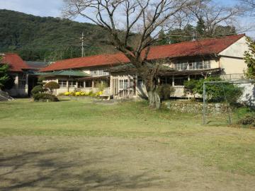 サッカーのゴールポストが設置され大きな木が立つ奥にある赤色の屋根の校舎棟の建物外観の写真