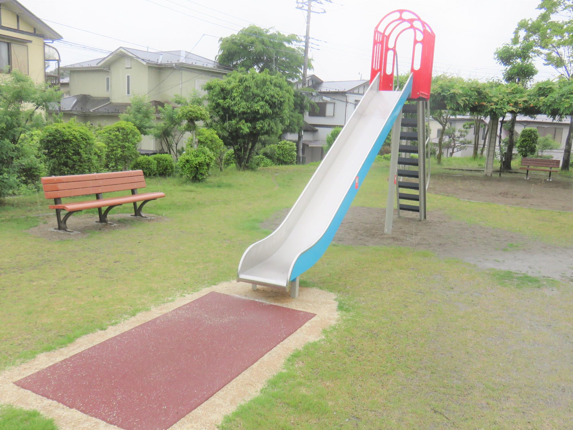 住宅街に囲まれた公園内に新しく設置されたベンチと滑り台の写真