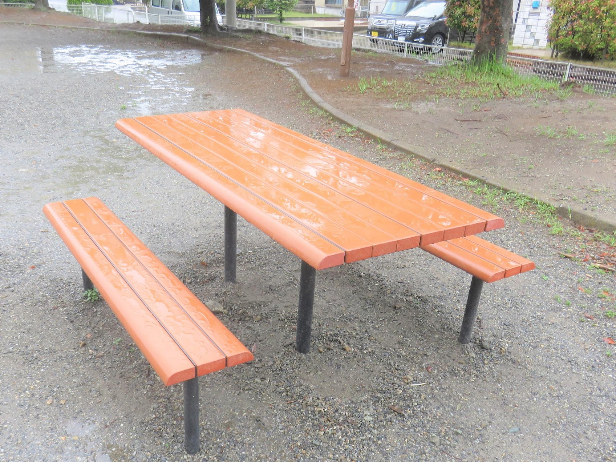 長方形のテーブルに2台の長椅子が公園内に設置された野外卓の写真