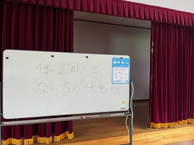 舞台の前に置かれたホワイトボードに「体調の良くない方の休憩所」と書かれているのを撮影した写真