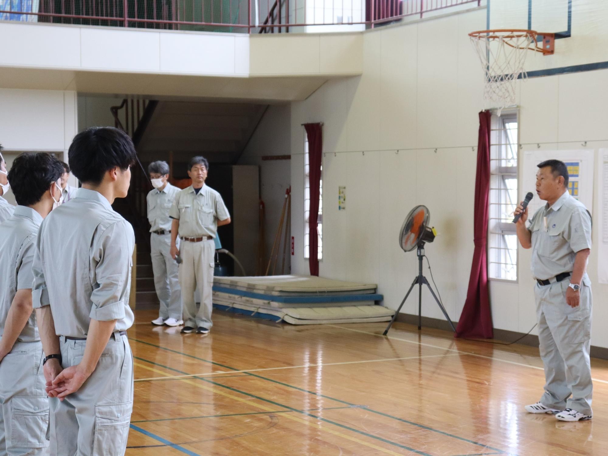 マイクを持った男性が参加者たちの前で話をしている写真