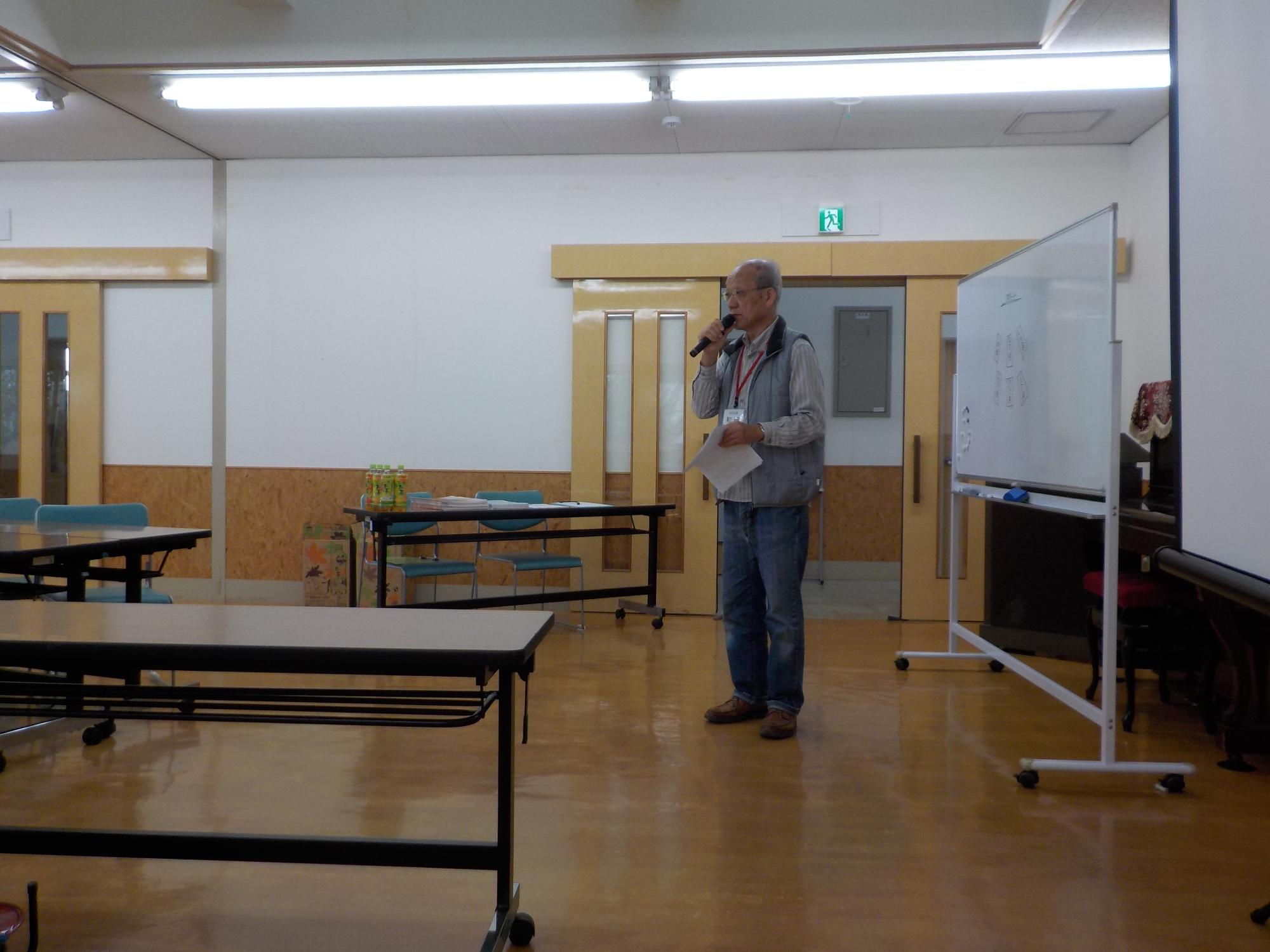 部屋の中でマイクを持った男性が立って話をしている写真