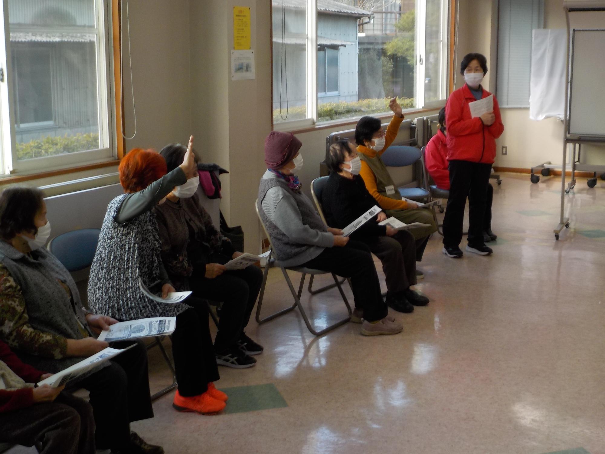 窓際に並んだパイプ椅子に座る参加者の皆さんが積極的に手を挙げて講和に参加している様子を撮影した写真