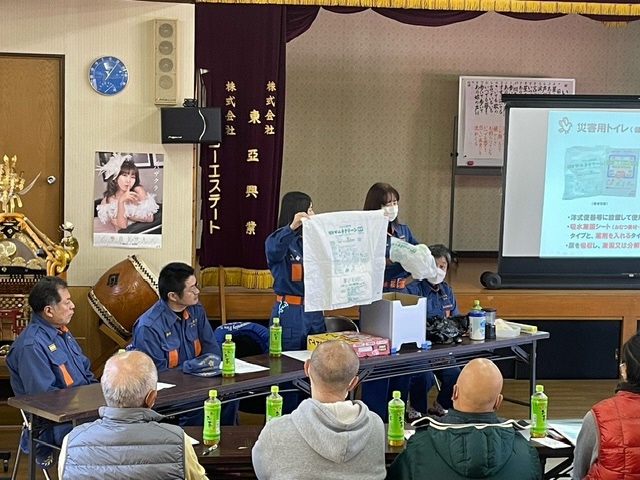 消防団の団員たちが防災グッズを手に持って参加者たちに紹介している写真