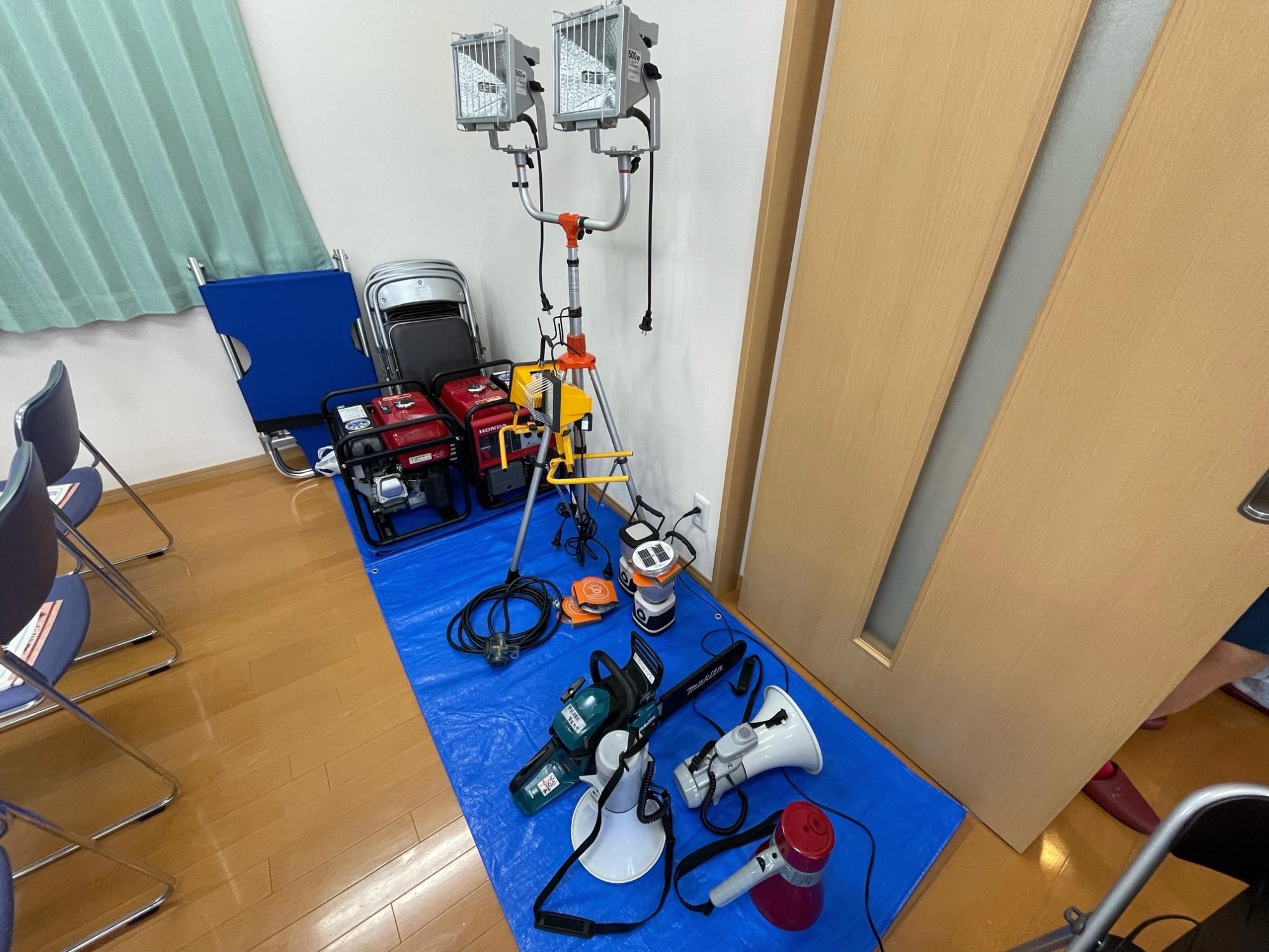 複数の拡声器やスタンドつきライトなどが部屋のすみに集めて置かれている写真