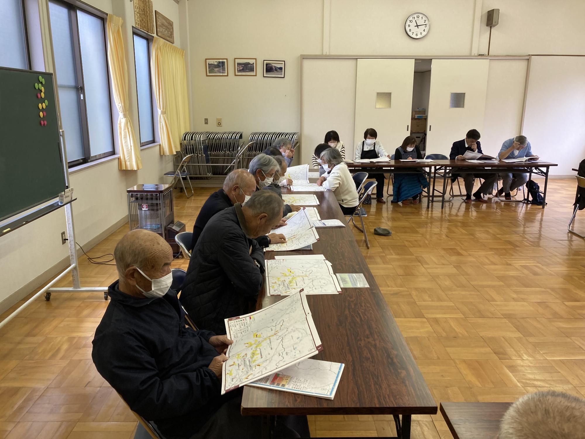 男性4人が並んで座るテーブルの上には置かれていているハザードマップを熱心に見ている様子を横から撮影した写真